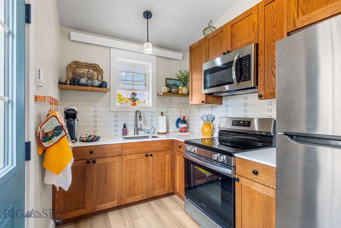 Kitchen with honey-colored wood cabinets, stainless steel appliances, and a window above the sink.