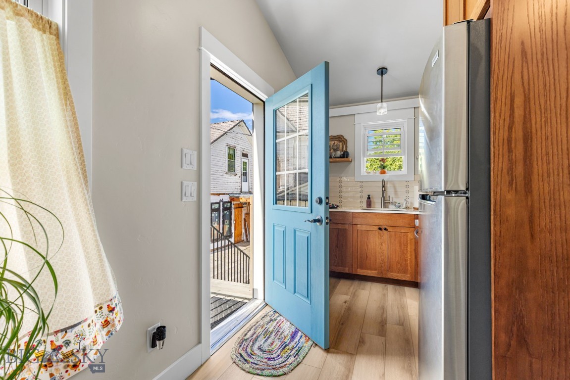 Kitchen with wood cabinets and stainless refrigerator, viewed through an open blue door.