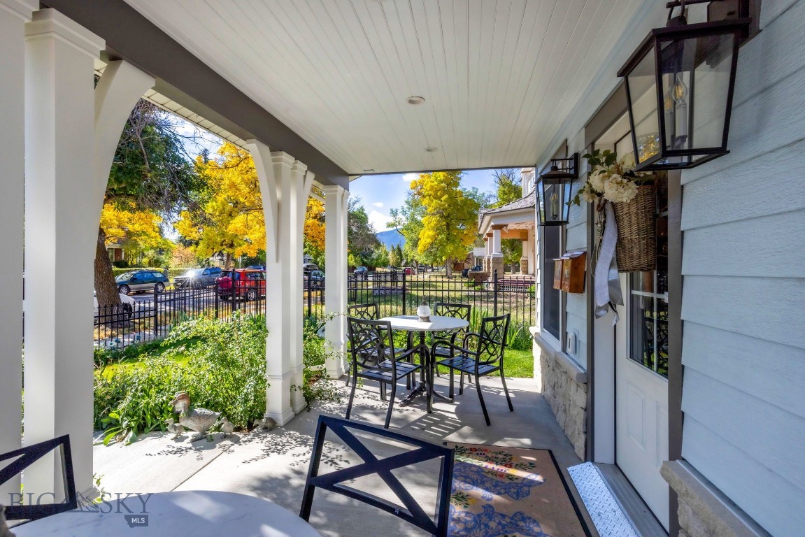 Covered porch with black dining set, garden beds, and yellow autumn trees beyond the fence.