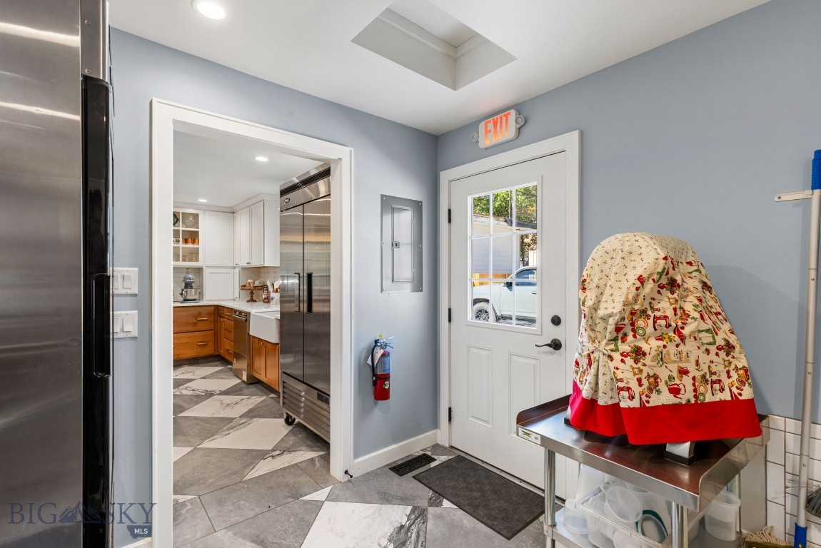 Commercial kitchen entry with a stainless worktable, covered equipment, and a white-paned exit door.