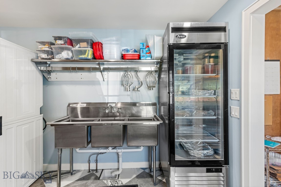 Commercial kitchen with a stainless-steel three-compartment sink and glass-door refrigerator.