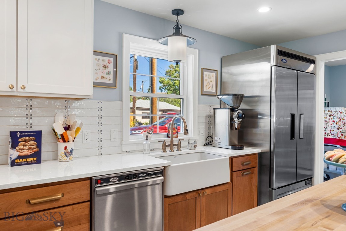 Kitchen with farmhouse sink, white countertops, wood cabinets, and stainless-steel refrigerator.