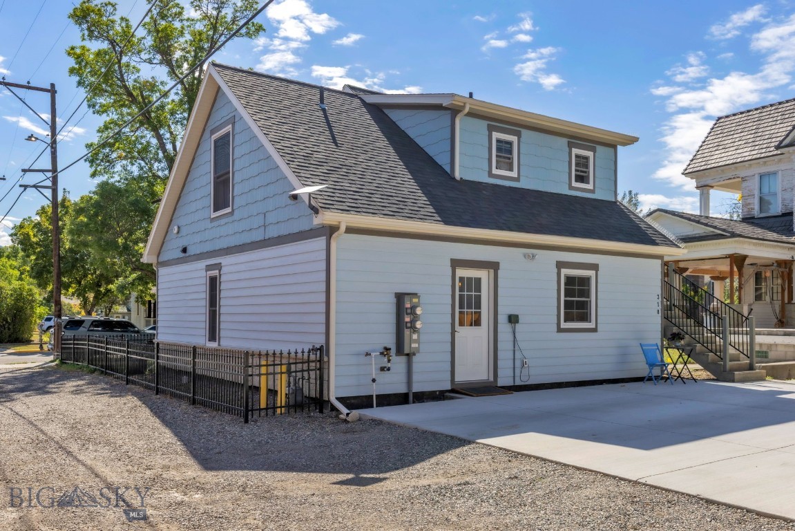 Light blue two-story house with steep shingle roof, fenced gravel yard, and concrete driveway.