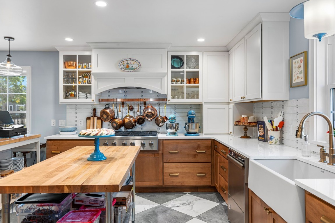 Kitchen with a butcher-block island, copper pots, white cabinets, and a farmhouse sink.