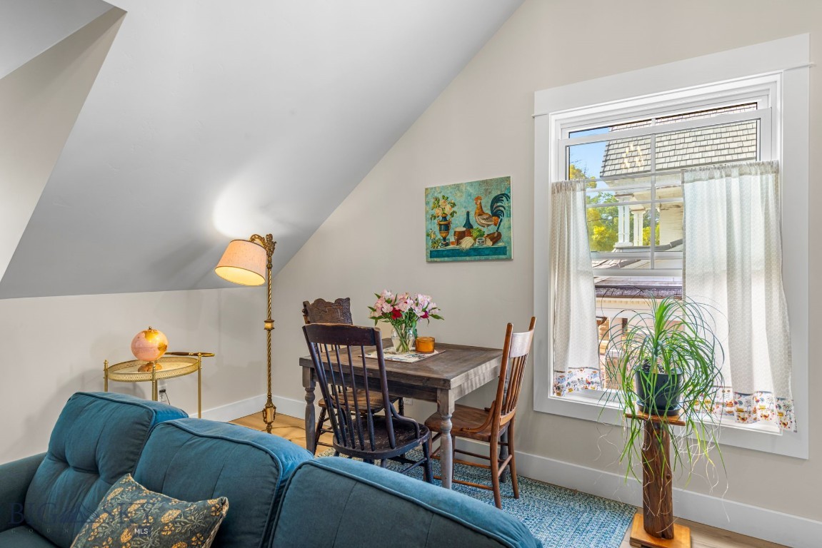 Attic living and dining area with a blue sofa, wooden table, and curtained window.
