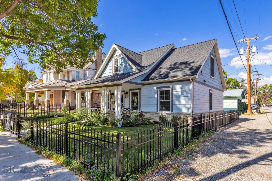 Blue-gray gabled house with a covered porch and fenced garden beside a neighboring home.