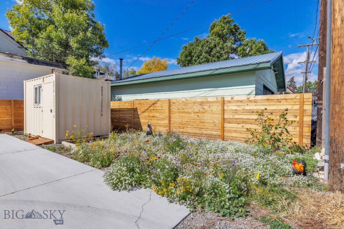 Fenced side yard with a wildflower garden, concrete walkway, and light-colored storage container.
