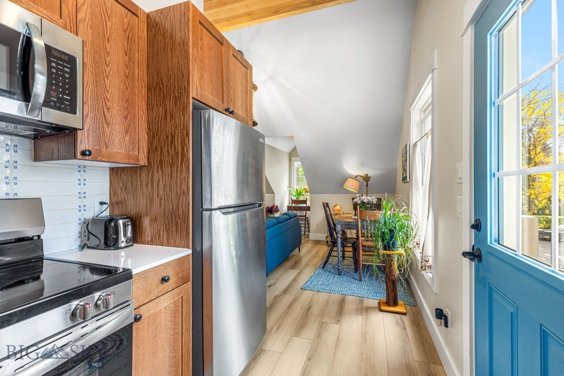 Kitchen and dining area with warm wood cabinets, stainless appliances, and a bright blue exterior door.