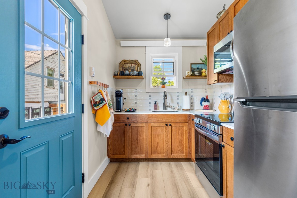 Compact kitchen with warm wood cabinets, stainless steel appliances, and a turquoise-blue windowed door.