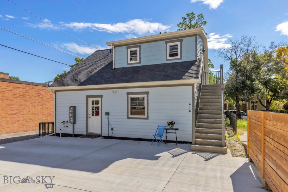 Light blue-gray home with a dark gambrel roof, exterior stairs, and a broad concrete patio.