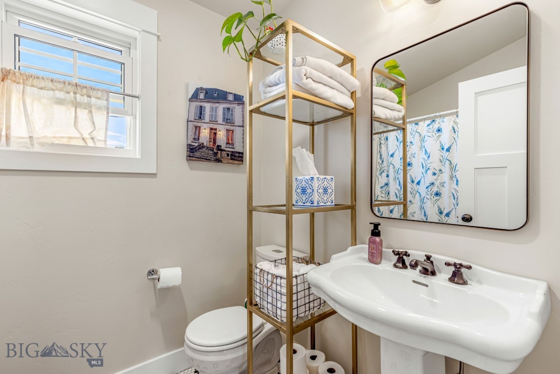 Bathroom with a white pedestal sink, gold-tone towel shelving, and a blue floral shower curtain.