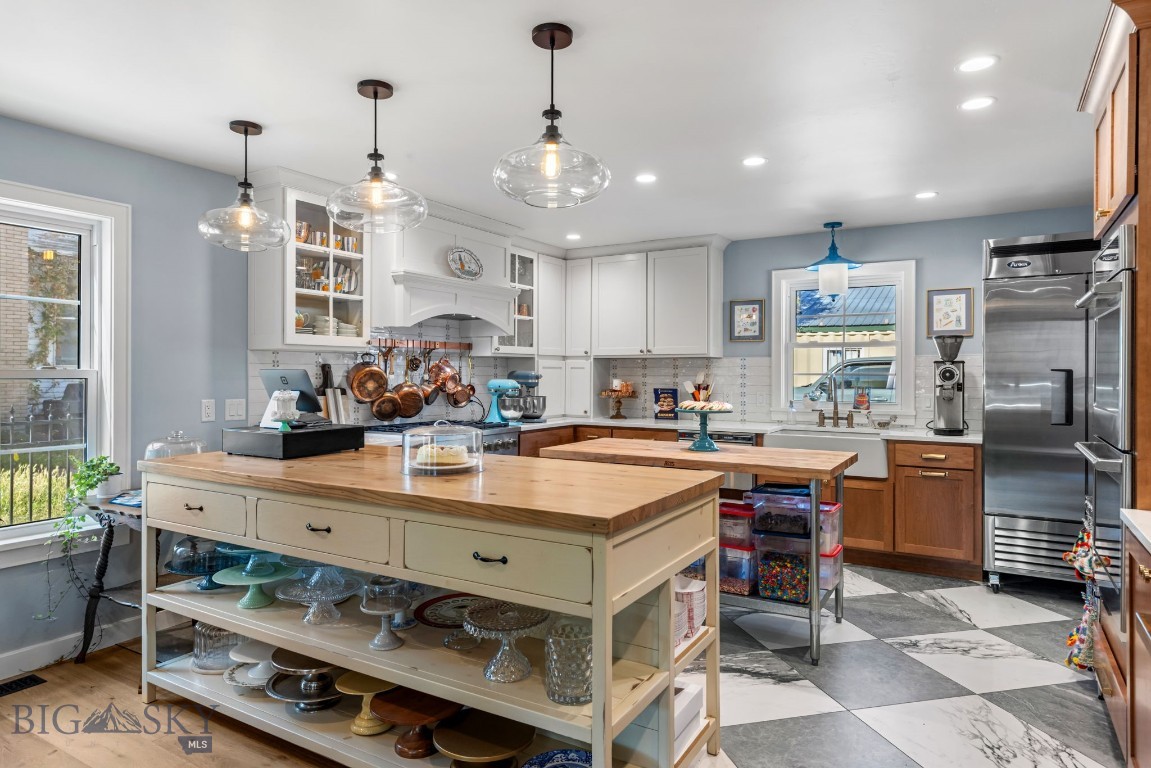 Kitchen with a large wooden island, white cabinetry, stainless appliances, and checkered flooring.