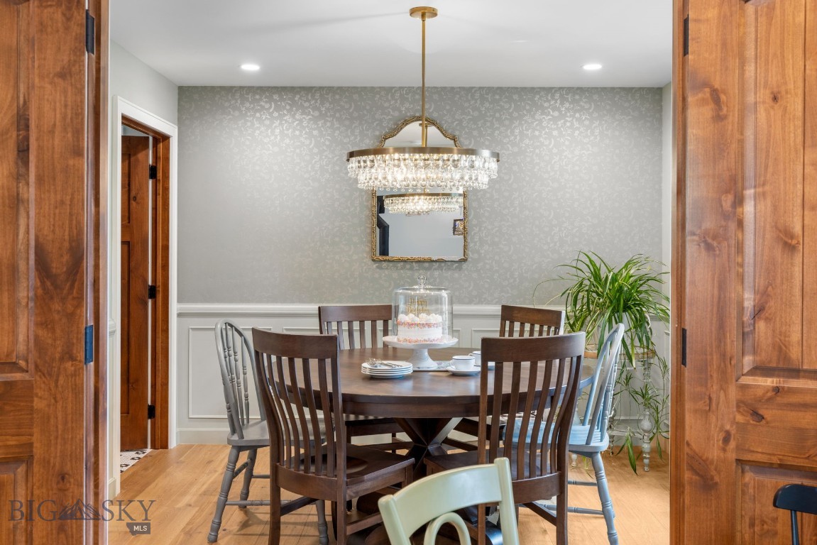 Dining room with a round wood table, crystal chandelier, and patterned gray wallpaper.