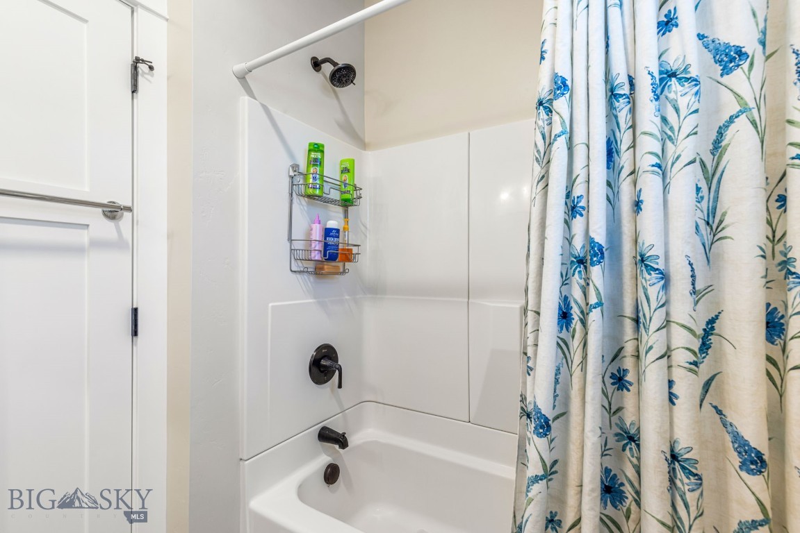 Bathroom tub and shower with dark fixtures, a toiletry caddy, and a blue floral curtain.