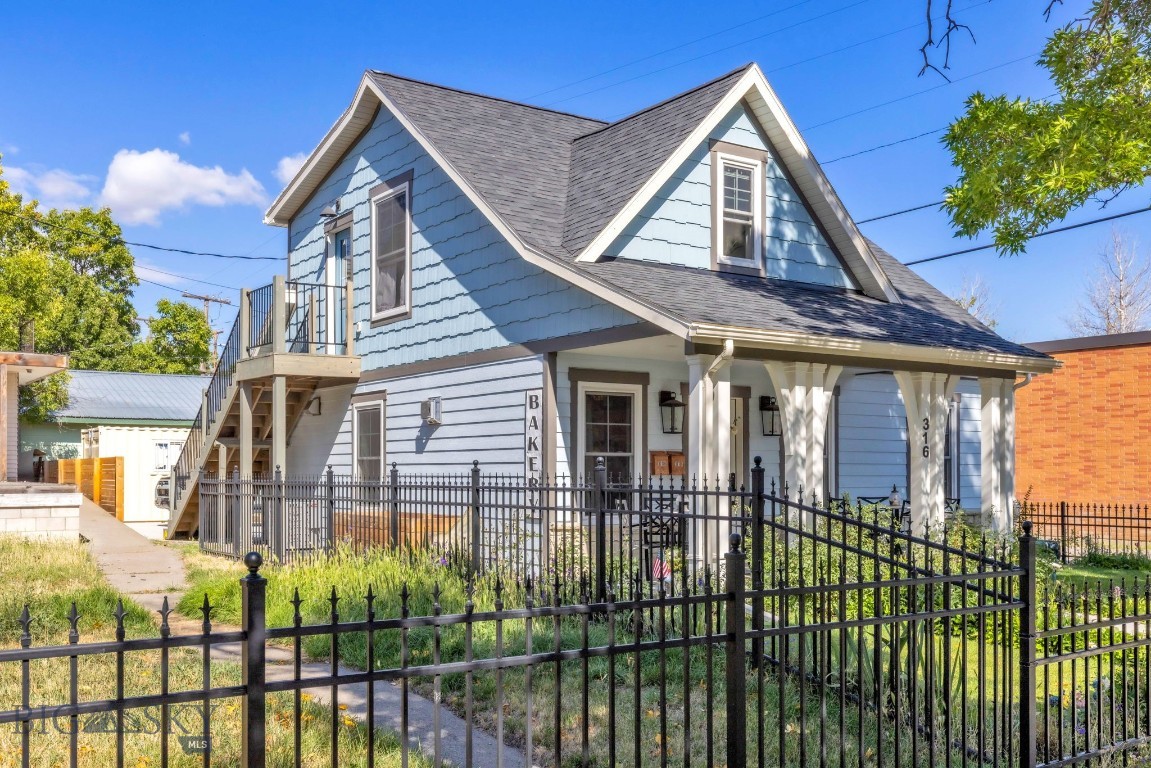 Blue two-story house with steep gabled roofs, an upper balcony, covered porch, and black metal fence.
