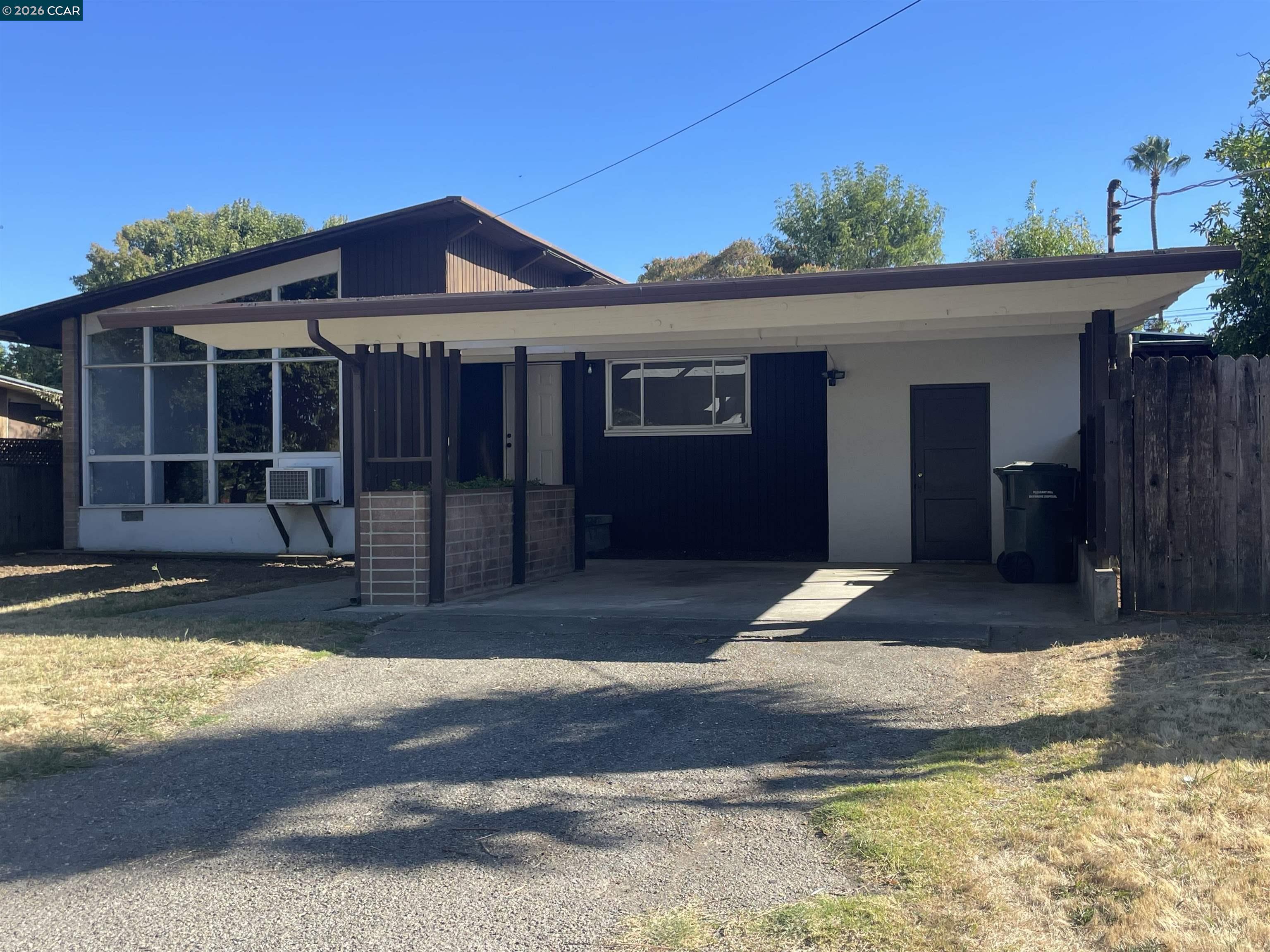 Modern single-story home with a broad carport, large windows, and a fenced yard.