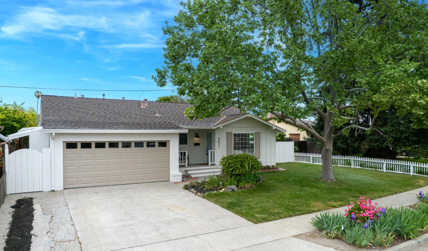 Single-story white house with a beige double garage door, broad driveway, and mature tree shading the lawn.