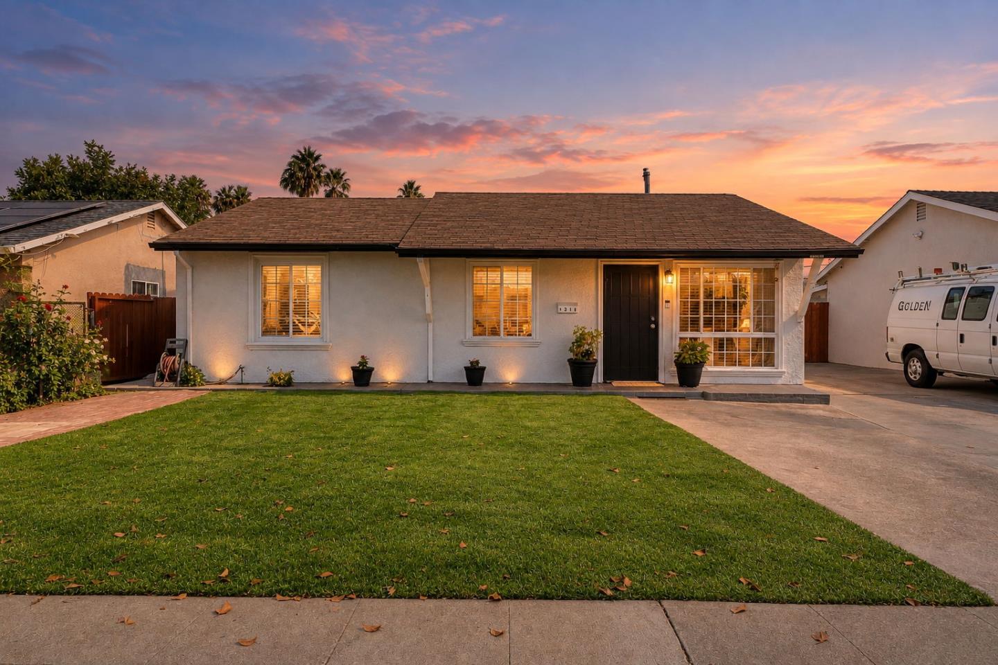 Single-story house with a broad front lawn and glowing windows at sunset.