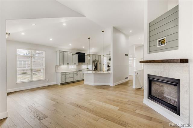 Vacant open-plan kitchen and living area with gray cabinetry, pale wood floors, and a fireplace.