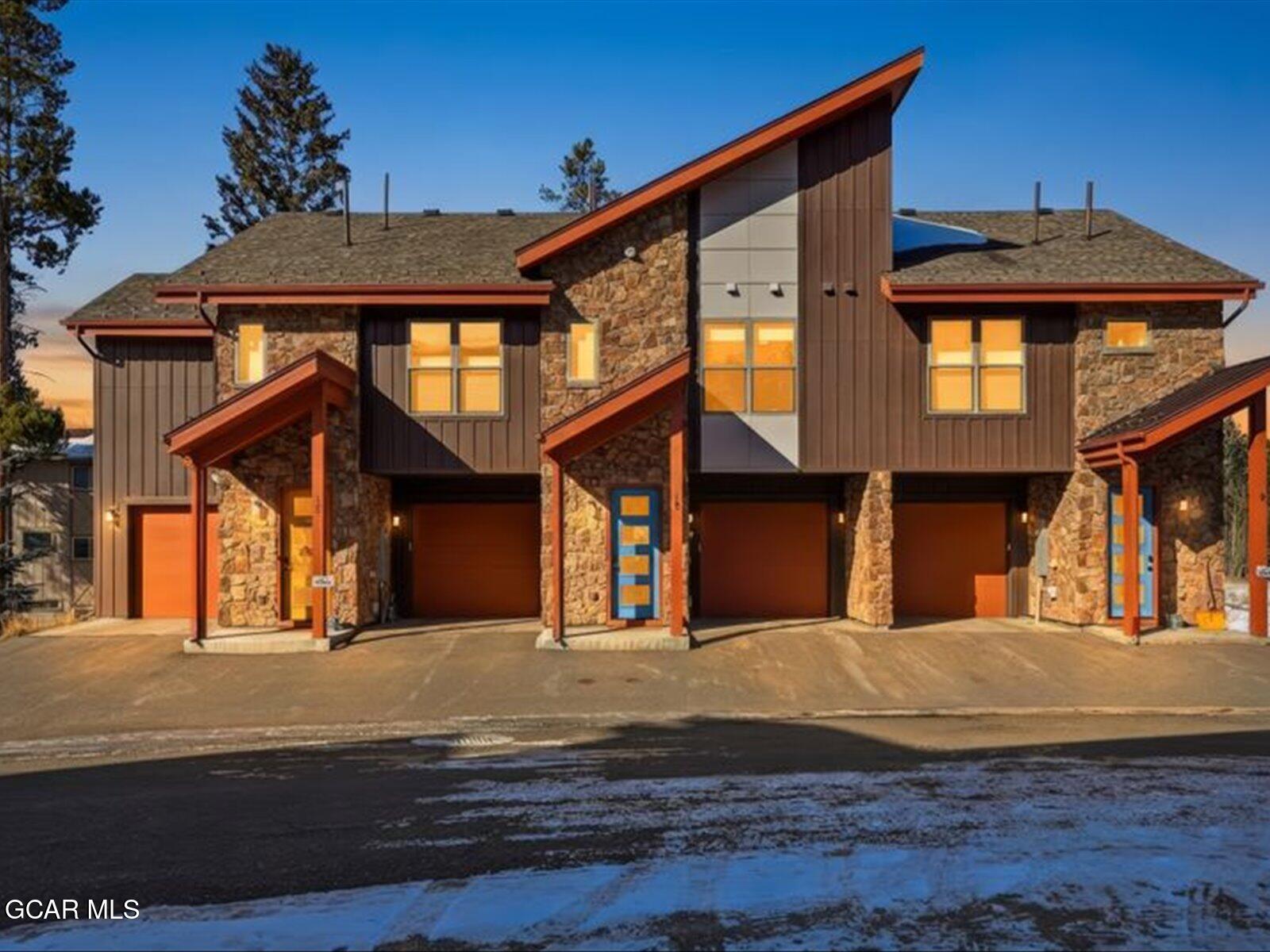 Modern stone-and-siding home with angular orange-red rooflines and blue doors.