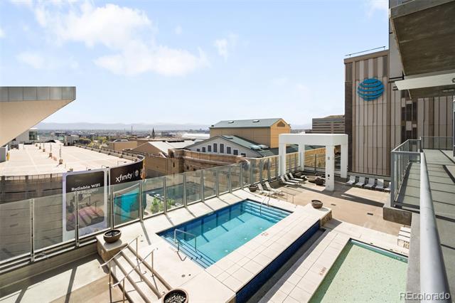 Rooftop pool and spa beside glass railings, with Denver buildings and mountains in the distance.