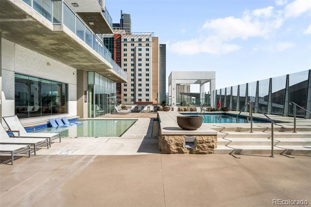 Rooftop pool deck with lounge chairs and surrounding high-rise buildings.