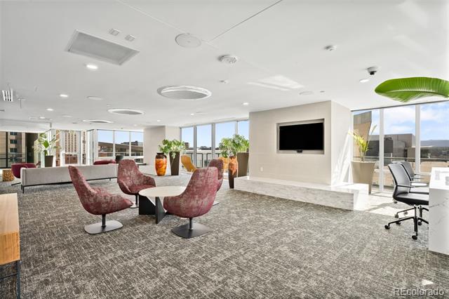 Condominium lounge with burgundy chairs, a wall-mounted television, and expansive windows.