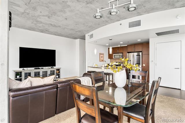 Open-plan condo living and dining area with a glass table, leather sofa, and wood-cabinet kitchen.
