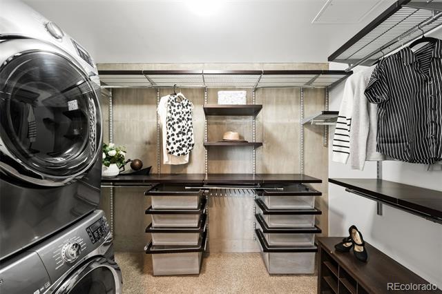 Walk-in closet with built-in storage, hanging clothes, shoe shelves, and a stacked washer and dryer.