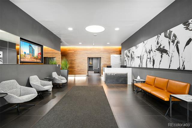 Modern condominium lobby with a reception desk, gray lounge chairs, and an orange leather sofa.