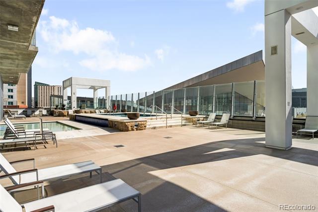 Rooftop pool terrace with lounge chairs, glass walls, and city buildings beyond.