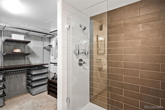 Walk-in closet beside a glass-enclosed shower with contrasting white and brown tile.