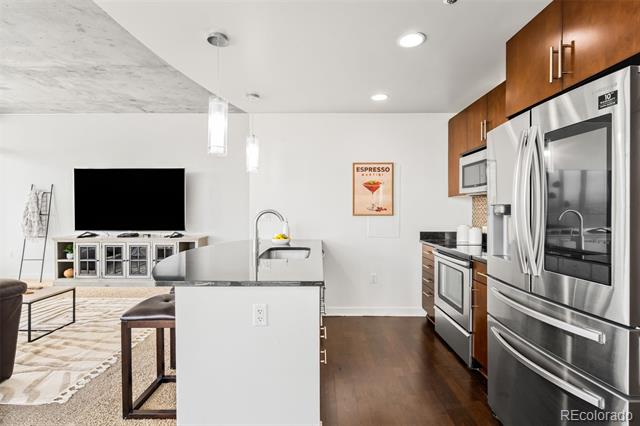Open-plan kitchen with a granite island, stainless steel appliances, and warm wood cabinets.