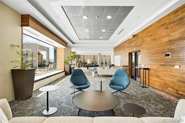 Condominium lobby lounge with teal chairs, round tables, and a long wood-paneled wall.