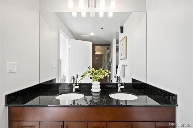Bathroom vanity with double sinks, a black stone countertop, and flowers between the sinks.