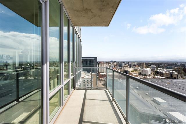 High-rise condo balcony overlooking the Denver skyline, with glass railings and floor-to-ceiling windows.
