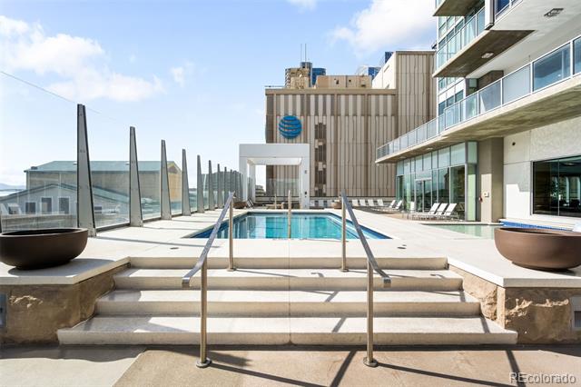 Rooftop pool with lounge chairs, glass railings, and surrounding modern high-rise buildings.