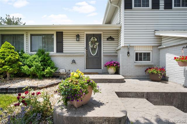 Light-gray two-story home with a dark front door, stone entry steps, and colorful flowers.