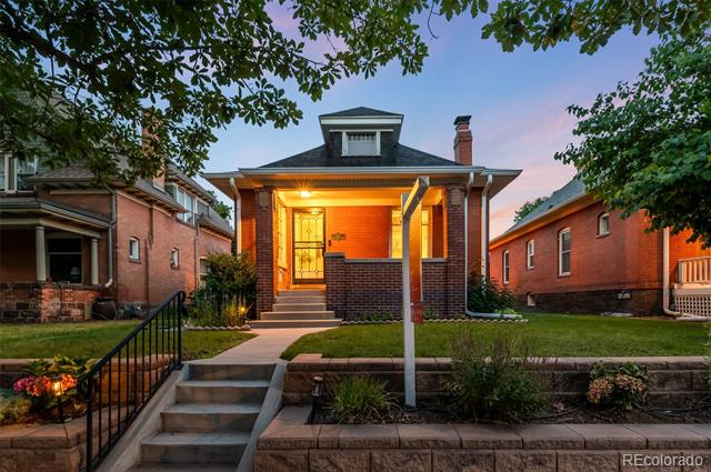 Red-brick home with a warmly lit porch, front steps, and mature trees at dusk.