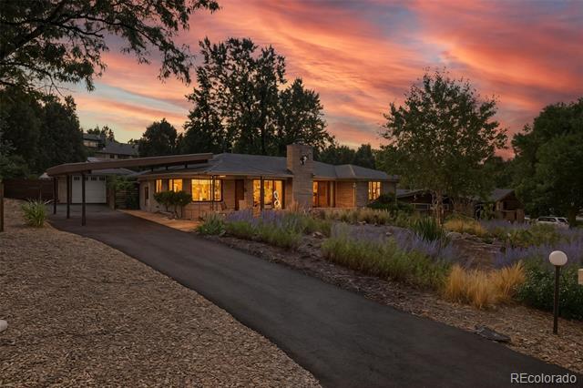 Modern single-story home with glowing windows and landscaped driveway at sunset.