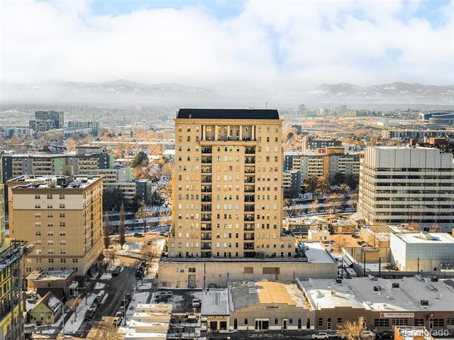 Tall tan apartment building rises above snow-dusted Denver streets, with mountains on the horizon.