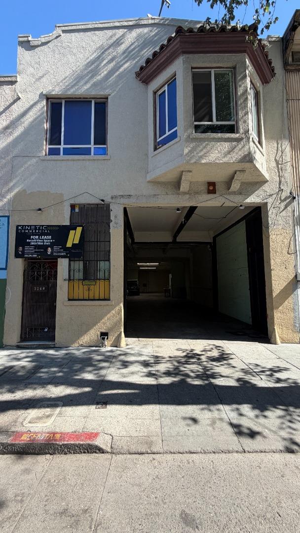 Two-story stucco commercial building with an open garage entrance and a Kinetic Commercial for-lease sign.