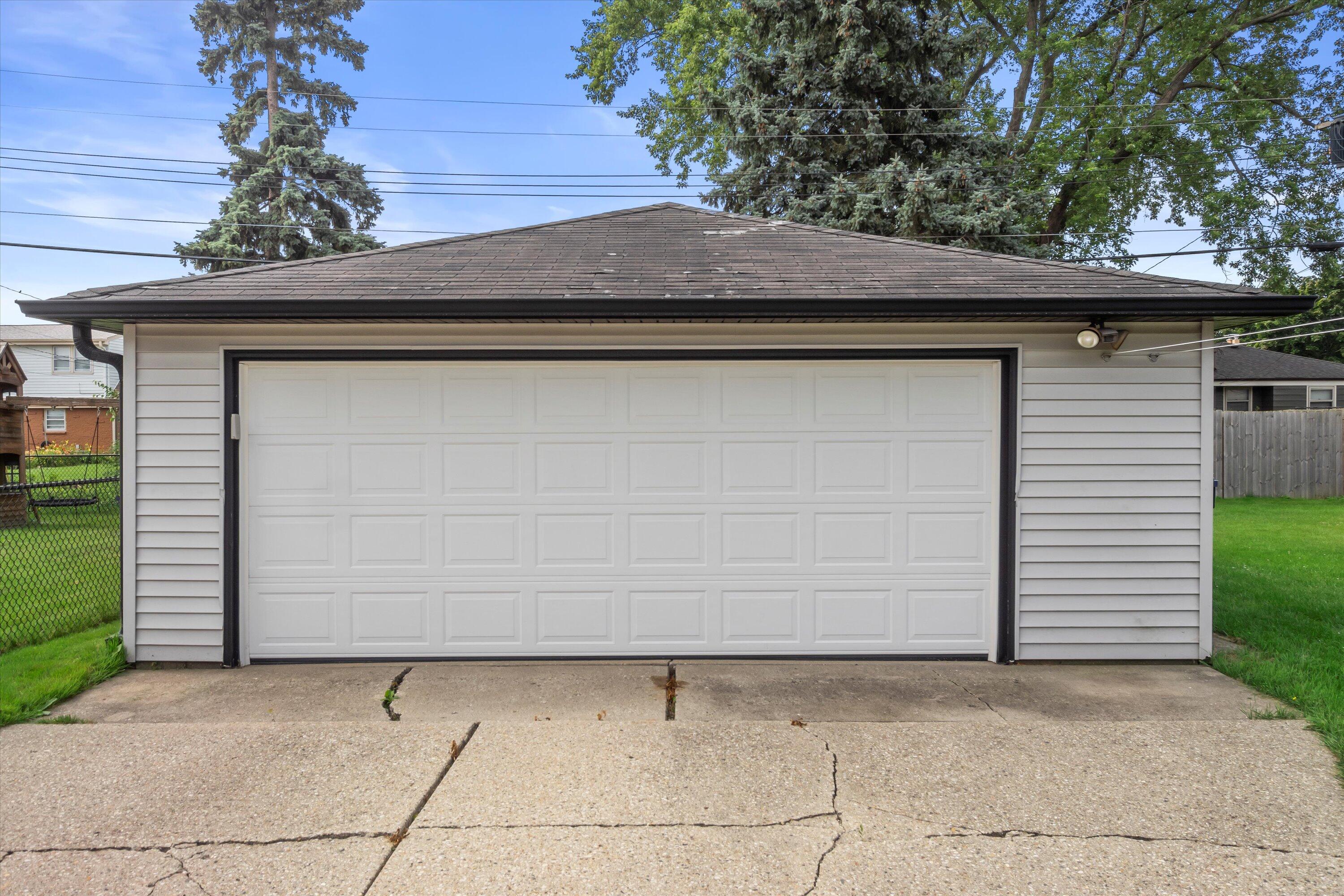 Detached garage with gray siding, a wide white paneled door, and a cracked concrete driveway.