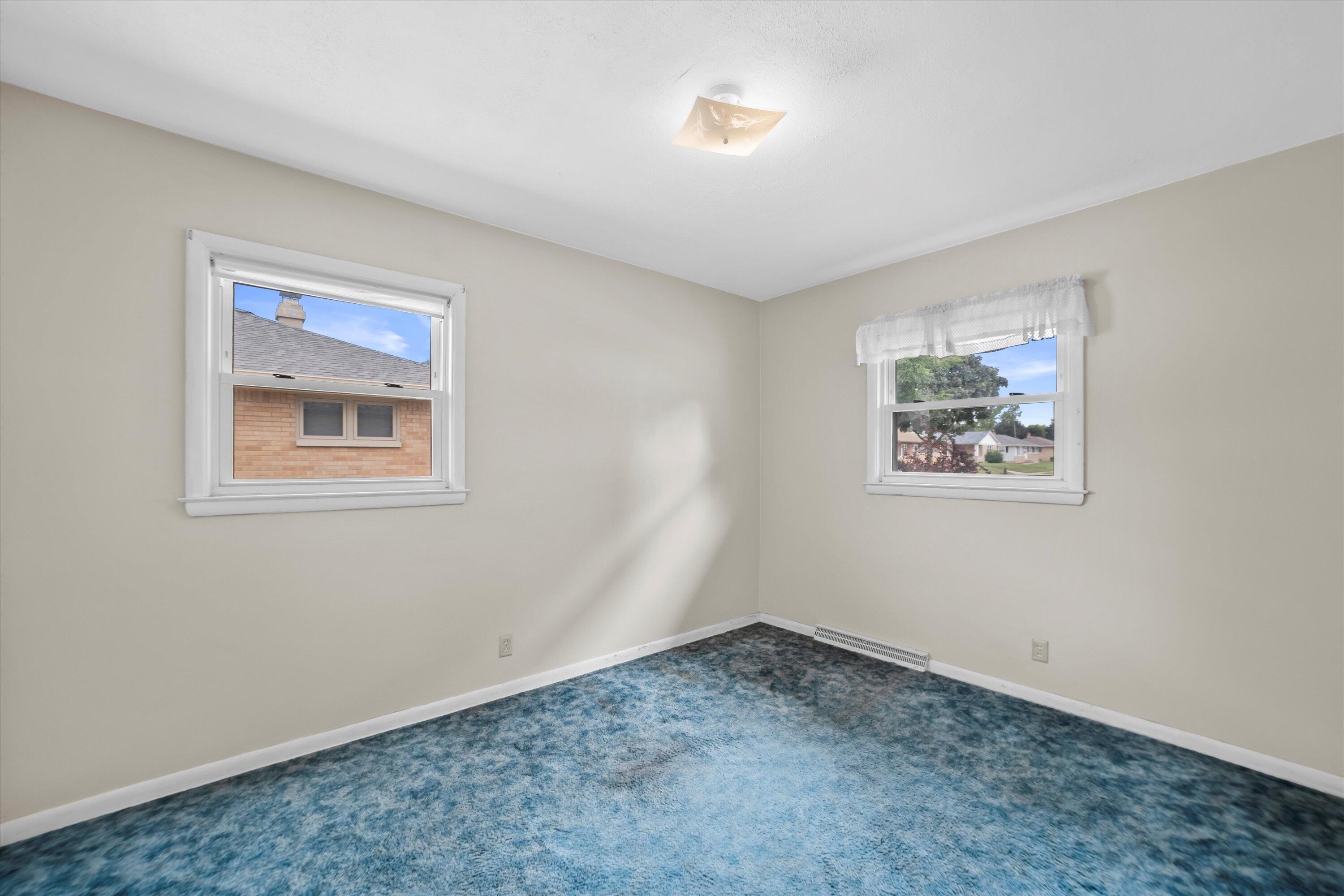 Empty bedroom with blue patterned carpet and two windows