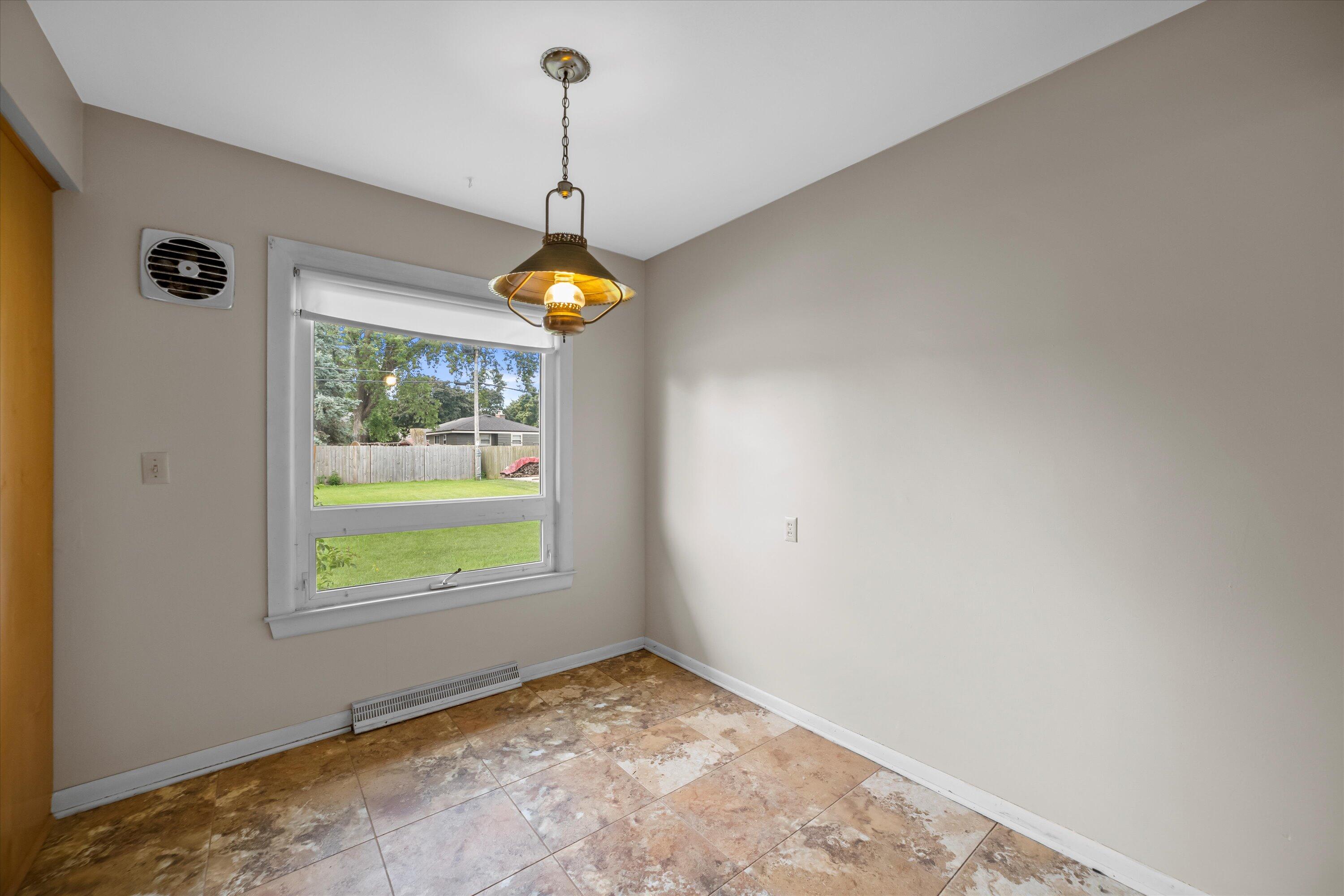 Empty tiled room with a hanging light and a large window overlooking the backyard.