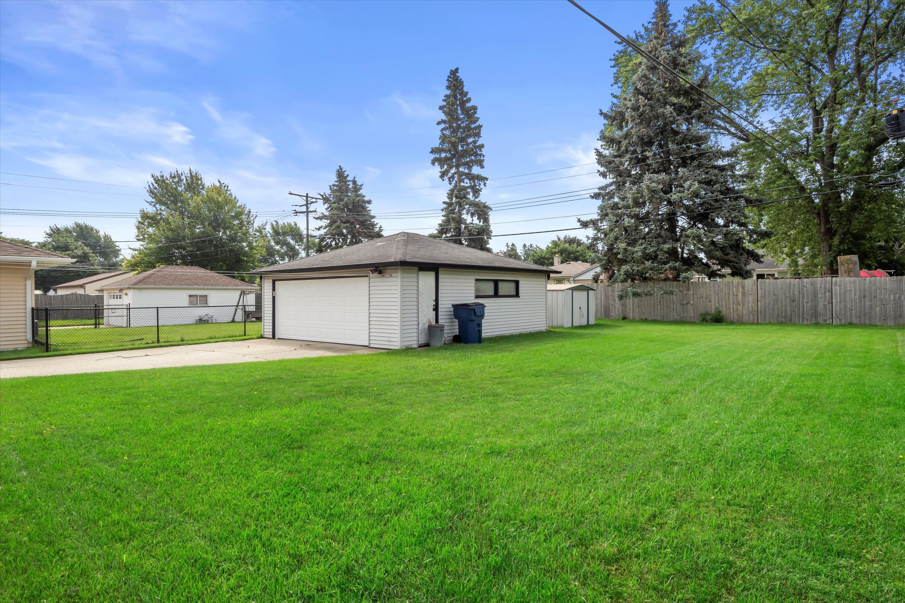 Detached white garage beside a broad green lawn, with a concrete driveway and fenced neighboring yards.