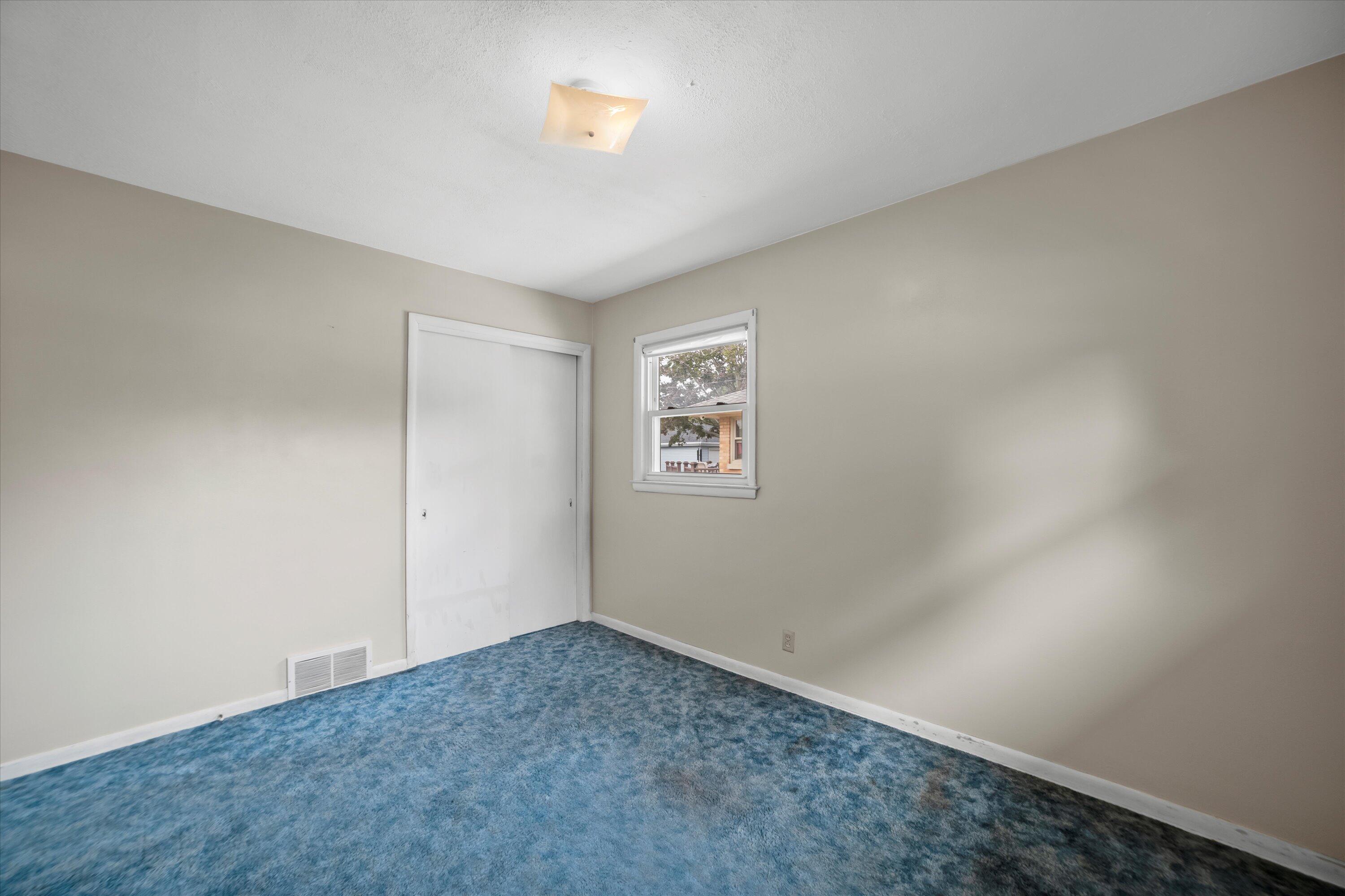 Empty bedroom with blue patterned carpet, a white sliding closet door, and a small window.