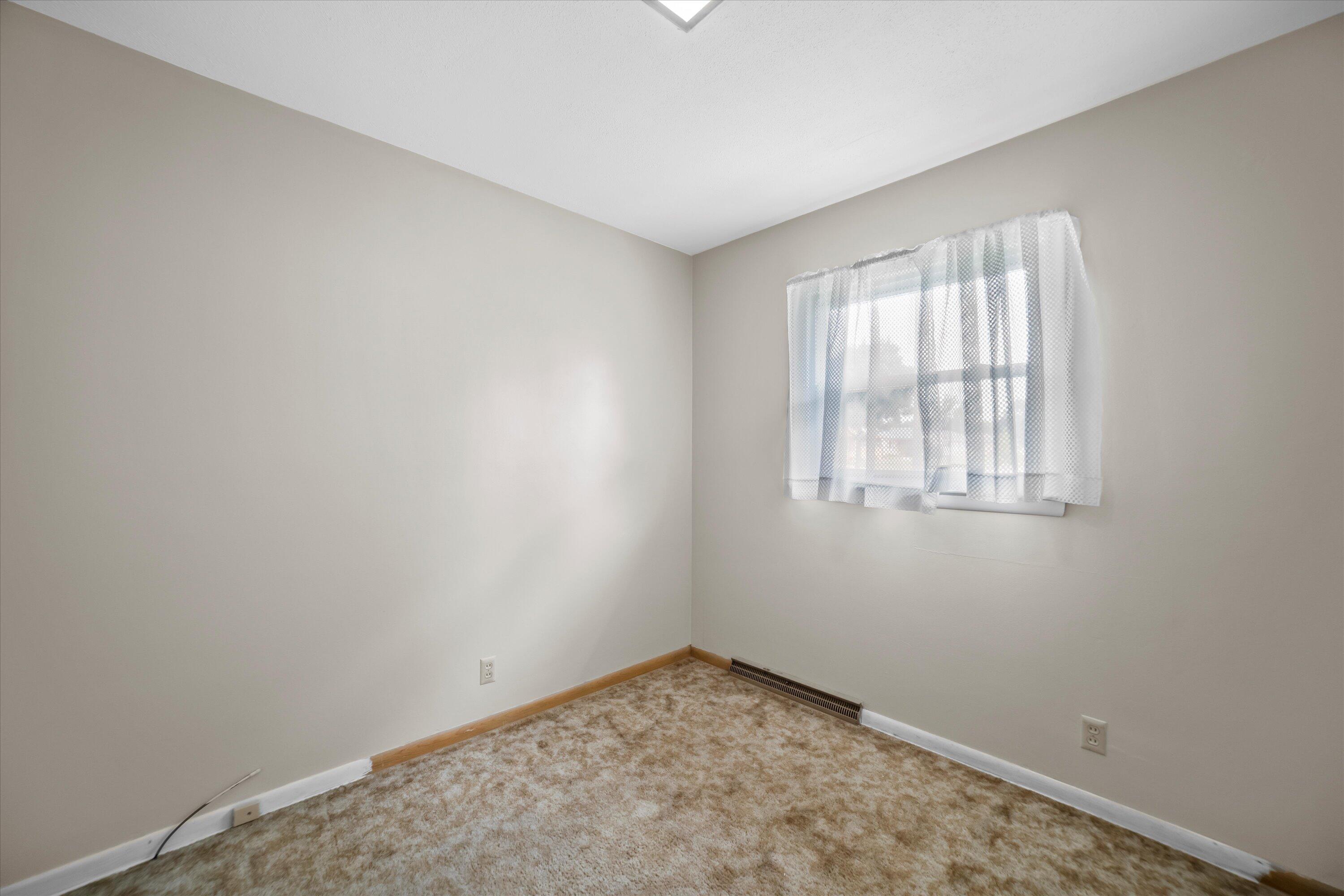 Empty bedroom with beige carpet and a curtained window.
