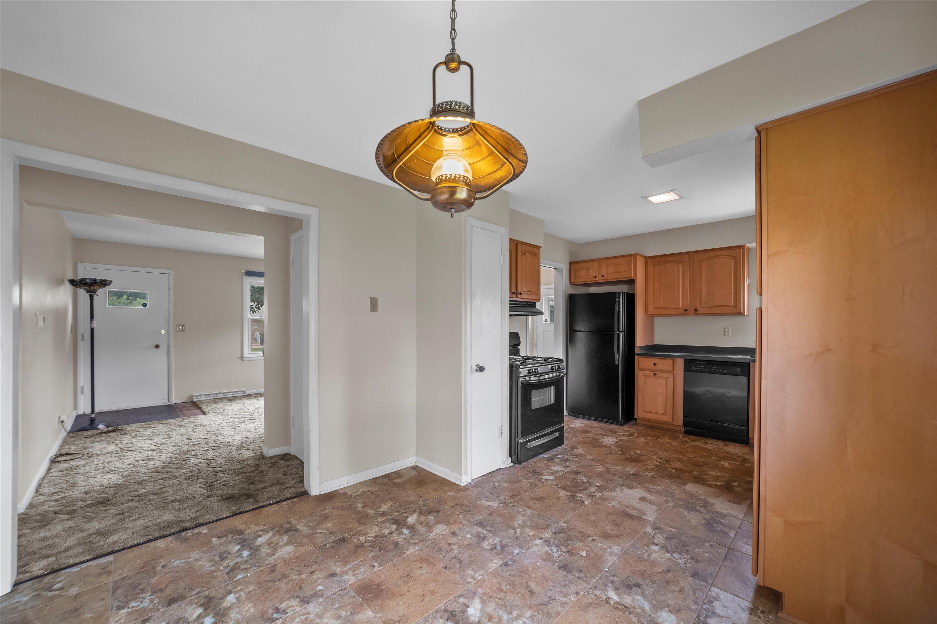 Kitchen with wood cabinets, black appliances, tiled floor, and a view into the carpeted entryway.
