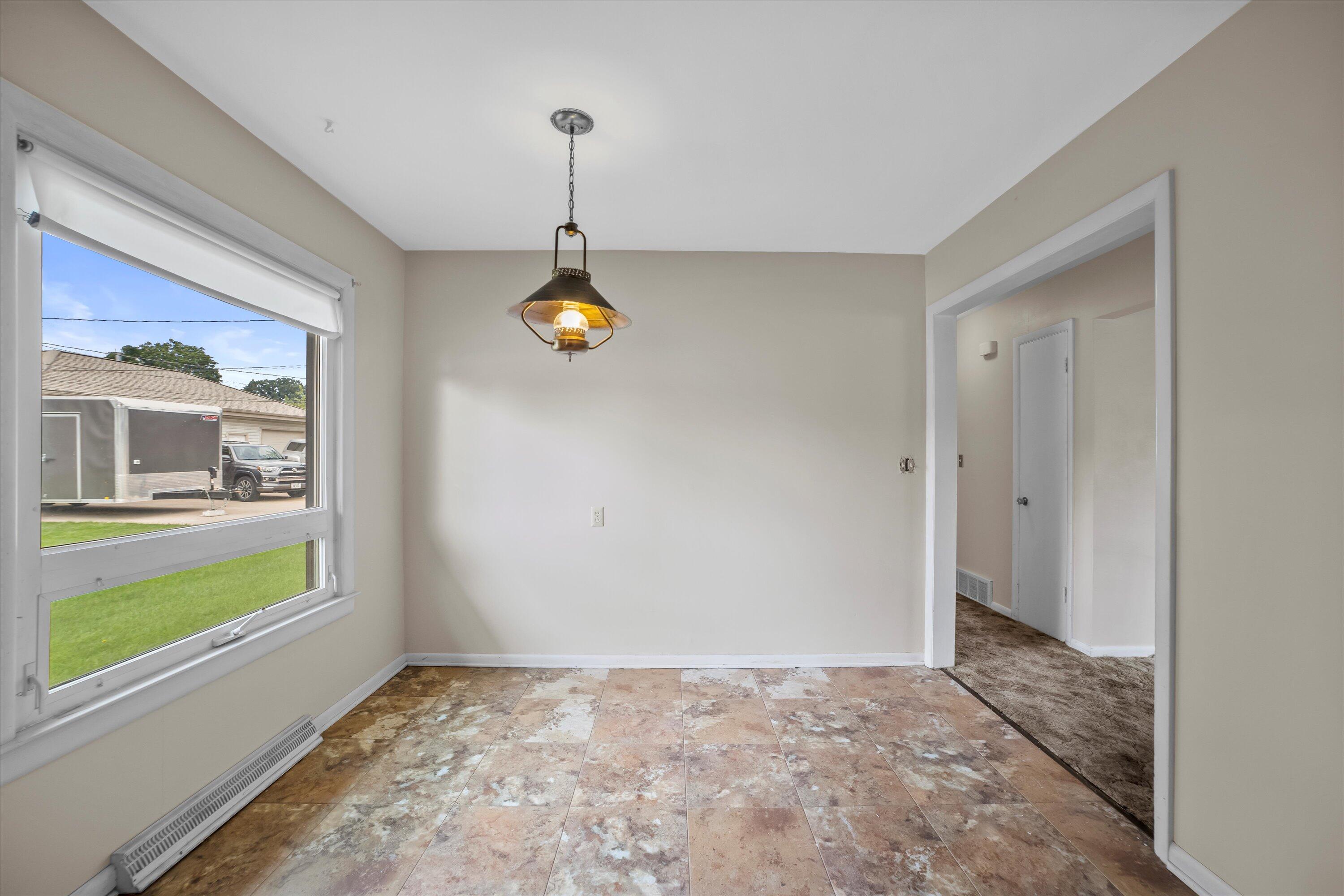 Empty dining area with mottled tile flooring, a large window, and a hanging pendant light.